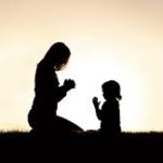 A woman and child are silhouetted against the sun.