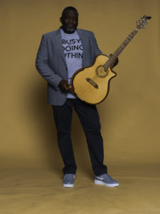 A man holding a guitar in front of an orange background.