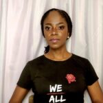 A woman wearing a black shirt with the words " we all " on it.